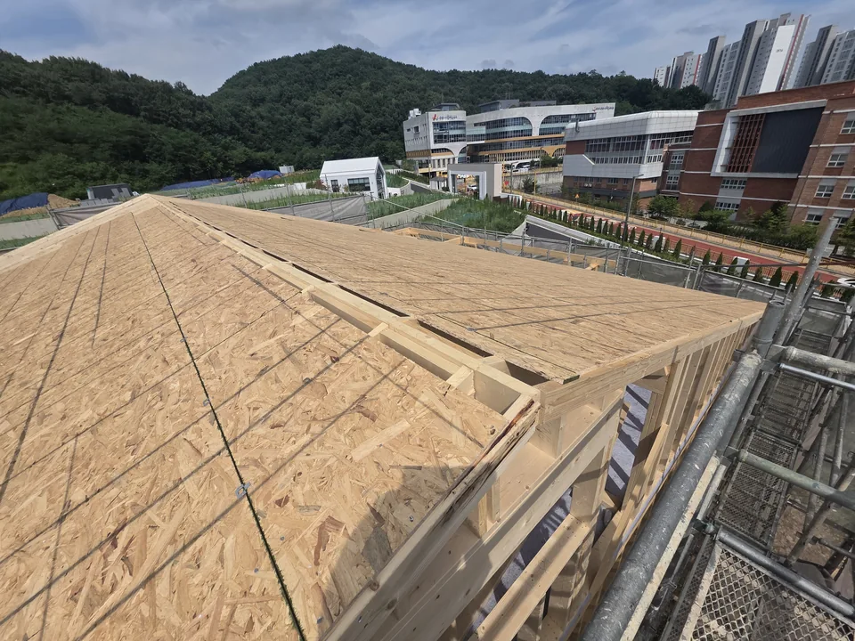 동탄 현장 지붕 합판 시공 — 산을 배경으로 한 지붕면